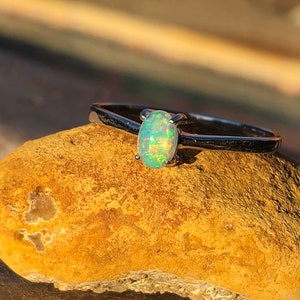 May include: A silver ring with a light green opal gemstone. The ring is sitting on a brown rock.