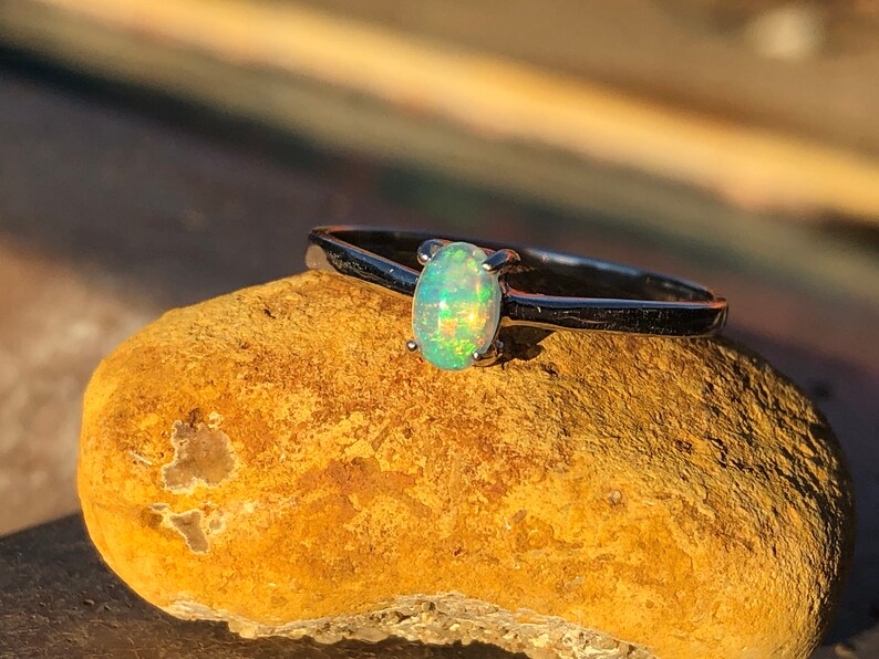 May include: A silver ring with a light green opal gemstone. The ring is sitting on a brown rock.