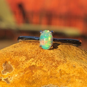 May include: A silver ring with a green opal gemstone. The ring is set on a rock.