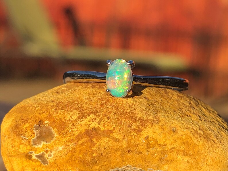 May include: A silver ring with a green opal gemstone. The ring is set on a rock.