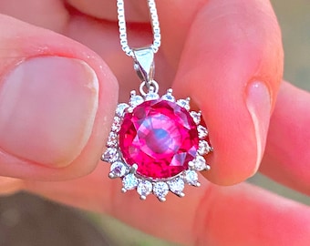 Op de afbeelding: Een zilveren ketting met een hanger van een roze edelsteen, omringd door een halo van kleinere, heldere edelstenen.