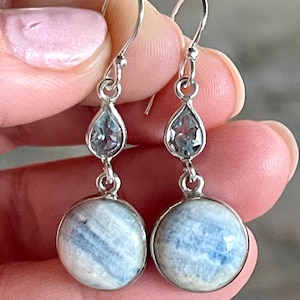 May include: Silver dangle earrings with a blue and white gemstone and a clear teardrop-shaped gemstone.