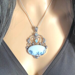 May include: A silver necklace with a white and black agate pendant. The pendant is set in a silver filigree design and features a small blue gemstone in the center.