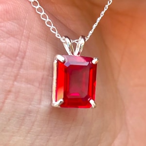 Puede incluir: Un collar de cadena de plata con un colgante de piedra roja. La piedra es de corte rectangular esmeralda.
