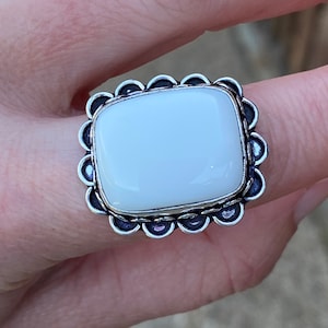 May include: A white gemstone ring with a silver setting. The ring has a scalloped edge and a square-shaped stone.