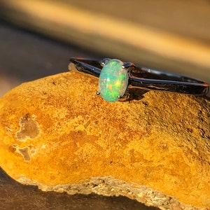 May include: A silver ring with a light green oval opal gemstone. The ring is sitting on a brown rock.