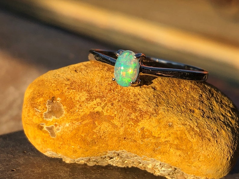 May include: A silver ring with a light green oval opal gemstone. The ring is sitting on a brown rock.