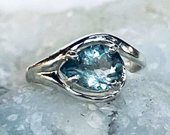 May include: A silver ring with a light blue gemstone set in a unique, curved design.