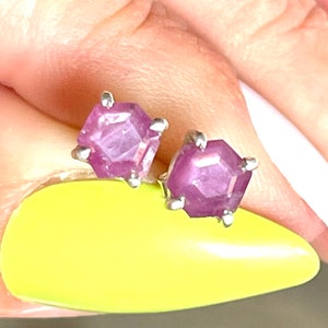 May include: A pair of silver stud earrings with pink gemstone accents. The gemstones are faceted and have a hexagonal shape.