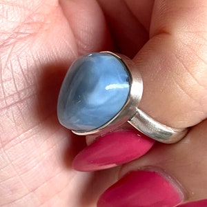 May include: A silver ring with a blue and white opal gemstone. The ring is set in a simple band.