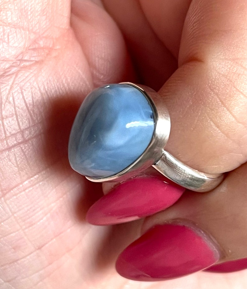 May include: A silver ring with a blue and white opal gemstone. The ring is set in a simple band.