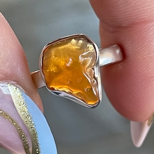 May include: A silver ring with a large, irregular, orange opal gemstone. The opal has a translucent, glassy appearance.