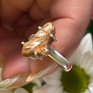 May include: A silver ring with a large, rough, copper-colored stone set in the center. The stone is irregularly shaped and has a textured surface.