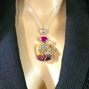 May include: A silver chain necklace with a pendant featuring a rectangular piece of agate with a tree design and a pink gemstone at the top.
