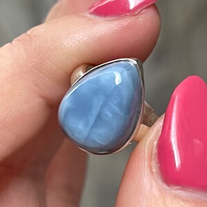 May include: A silver ring with a light blue opal gemstone. The opal has a pear shape and a smooth, polished surface.