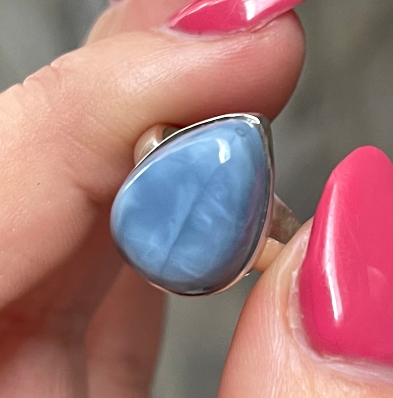 May include: A silver ring with a light blue opal gemstone. The opal has a pear shape and a smooth, polished surface.