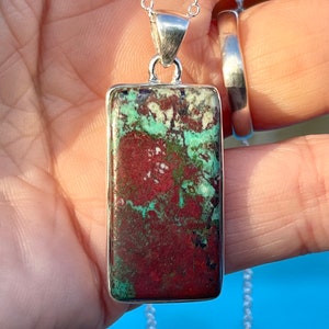 May include: A silver chain necklace with a rectangular pendant featuring a red, green, and white patterned stone.