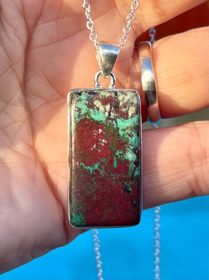 May include: A silver chain necklace with a rectangular pendant featuring a red, green, and white patterned stone.