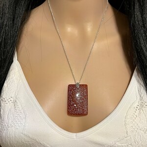 Può includere: Una collana con catena d'argento con un ciondolo rettangolare in agata marrone con venature bianche.