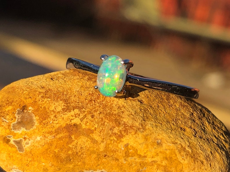 May include: A silver ring with a small oval opal gemstone. The opal is a light green color with flashes of rainbow.
