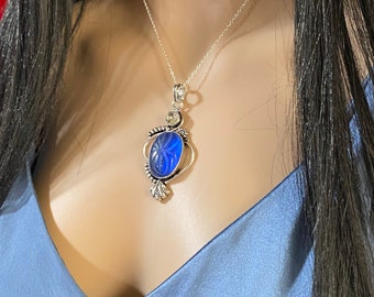 Peut inclure: Un collier pendentif en argent avec une grosse pierre précieuse bleue ovale et des détails argentés complexes. Le pendentif est suspendu à une fine chaîne en argent. Le collier est présenté sur un mannequin.