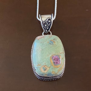 May include: A silver chain necklace with a pendant featuring a green, pink, and white gemstone set in a silver bezel. The pendant has a decorative silver bail.