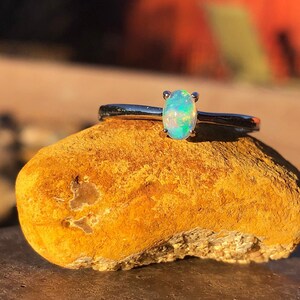 May include: A silver ring with a small oval opal gemstone. The opal is a light blue-green color with flashes of rainbow.