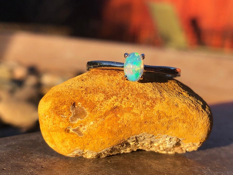 May include: A silver ring with a small oval opal gemstone. The opal is a light blue-green color with flashes of rainbow.