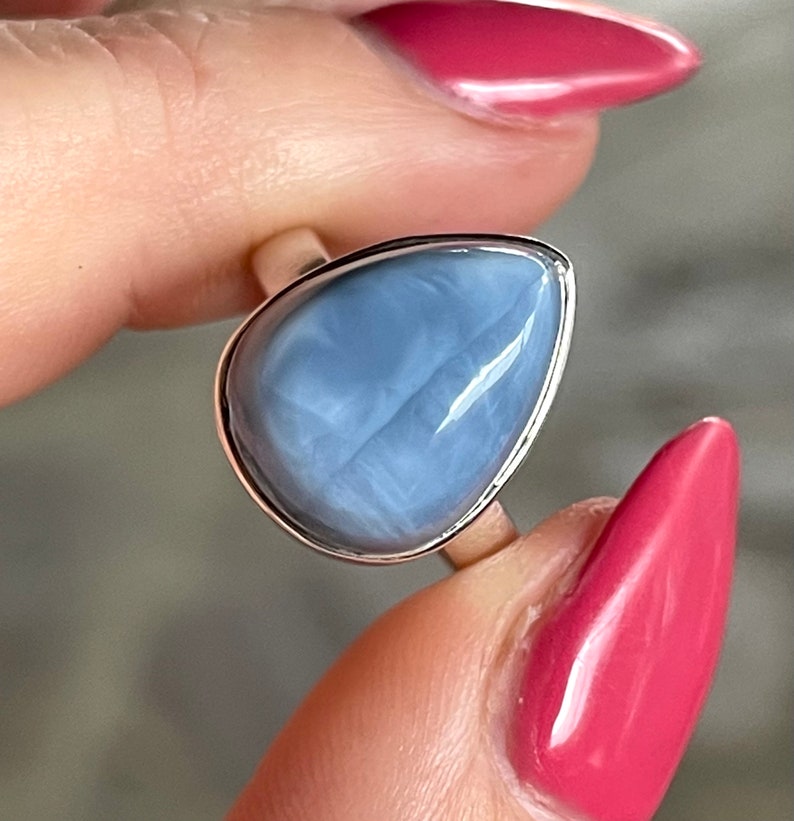 May include: A silver ring with a light blue teardrop-shaped opal gemstone.