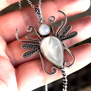 May include: Silver dragonfly pendant necklace with two white moonstone gemstones. The dragonfly has detailed wings and a beaded tail.