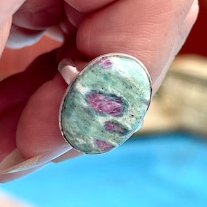 Op de afbeelding: Een zilveren ring met een ovale groene en roze edelsteen. De edelsteen heeft een draaiende roze en groene patroon.