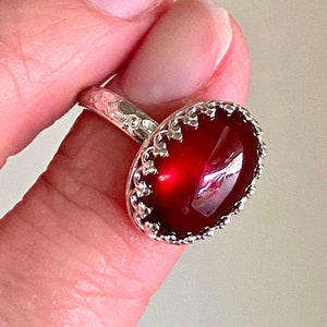 May include: A silver ring with a red gemstone set in a decorative crown-like setting.