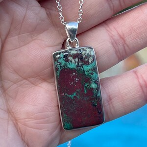 May include: A silver chain necklace with a rectangular pendant featuring a green, red, and white patterned stone.