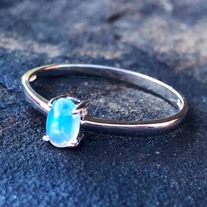 May include: A silver ring with a light blue oval opal gemstone.