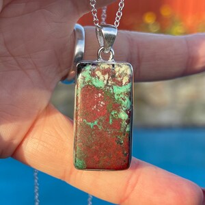 May include: A silver chain necklace with a rectangular pendant featuring a green and red stone. The stone has a mottled pattern.