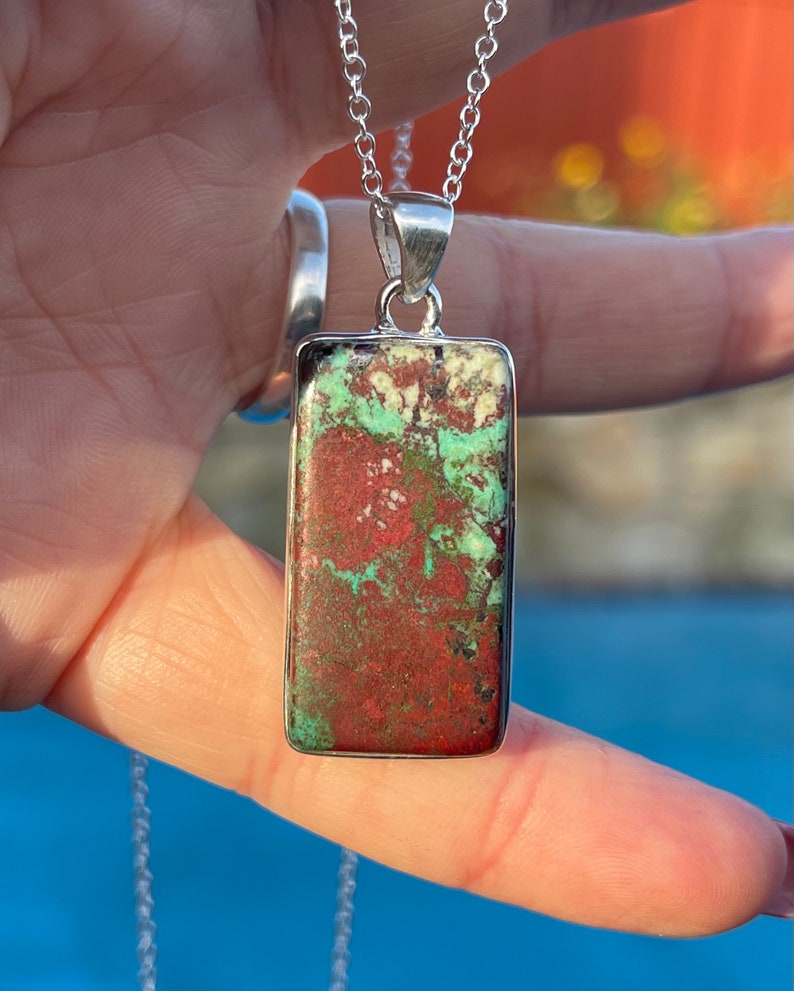 May include: A silver chain necklace with a rectangular pendant featuring a green and red stone. The stone has a mottled pattern.