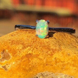 May include: A silver ring with a green opal gemstone set in a prong setting. The ring is resting on a yellow rock.