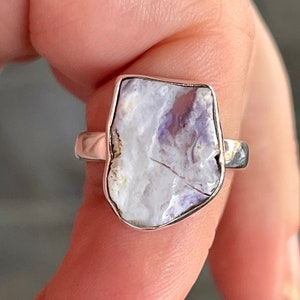 Può includere: Un anello d'argento con una grande pietra preziosa di forma irregolare, bianca e viola.