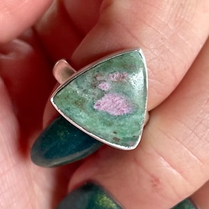 May include: A silver ring with a triangular green and pink gemstone. The gemstone has a unique pattern of pink and green.