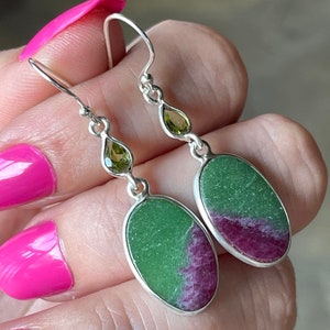 May include: A pair of silver dangle earrings with oval-shaped green and pink gemstones and smaller green pear-shaped gemstones.