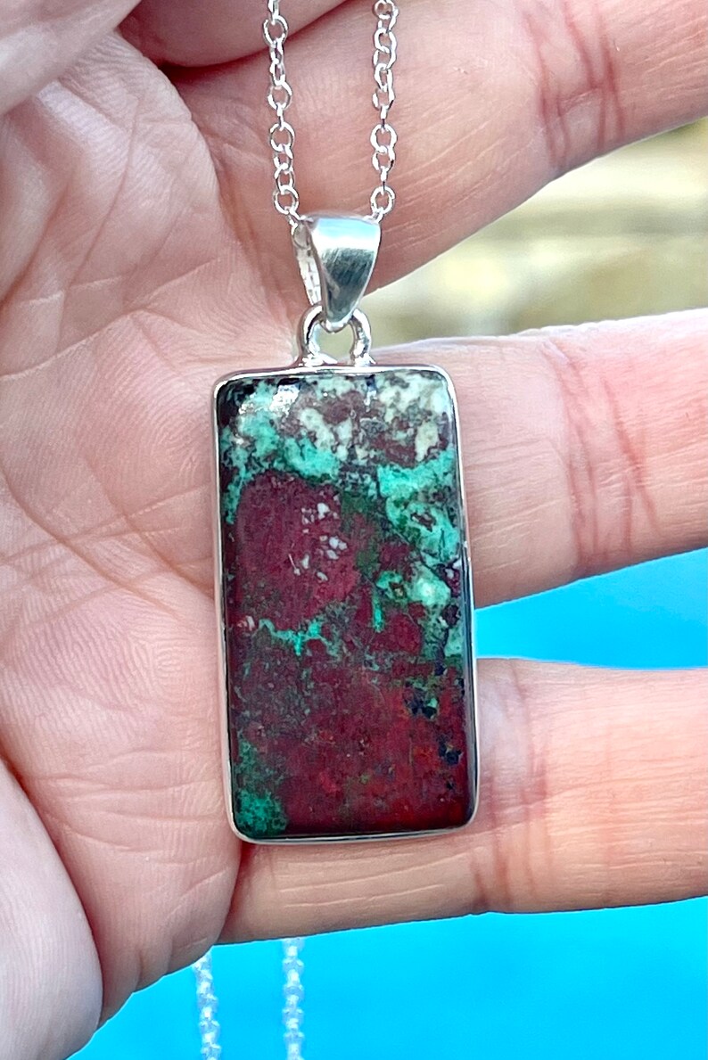 May include: A silver chain necklace with a rectangular pendant featuring a green and red jasper stone.