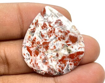 May include: A teardrop-shaped red and white agate cabochon with a swirling pattern. The stone is polished and has a smooth surface.
