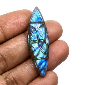 May include: A carved labradorite gemstone pendant with a blue and green iridescent sheen. The pendant is shaped like a teardrop and features a detailed butterfly design.