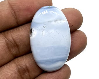 May include: A smooth, oval-shaped blue agate cabochon with white and gray banding. The stone has a light blue color with a subtle shimmer.