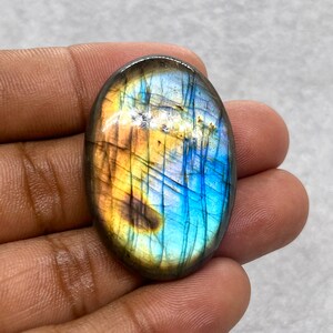 Puede incluir: Cabujón ovalado de labradorita con un brillo iridiscente azul, verde y dorado.