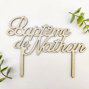 Peut inclure: Topper de g&acirc;teau en bois avec le texte "Bapt&ecirc;me de Nathan" en &eacute;criture cursive. Le topper est brun et a deux b&acirc;tonnets en bois pour l'ins&eacute;rer dans un g&acirc;teau.
