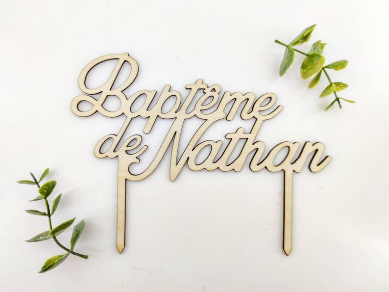 Peut inclure: Topper de g&acirc;teau en bois avec le texte "Bapt&ecirc;me de Nathan" en &eacute;criture cursive. Le topper est brun et a deux b&acirc;tonnets en bois pour l'ins&eacute;rer dans un g&acirc;teau.