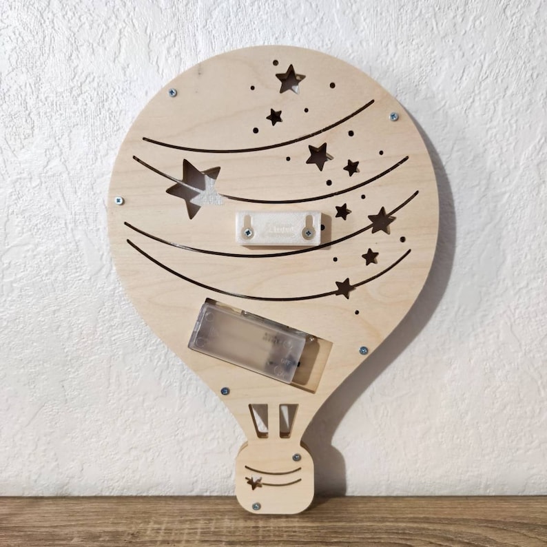 May include: A wooden hot air balloon night light with a battery pack and a string of stars cut out. The balloon is painted in a light wood colour and has a white battery pack.