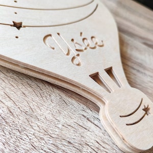 May include: A wooden hot air balloon ornament with the word "Alyssa" carved into it. The balloon has a star design on the bottom.