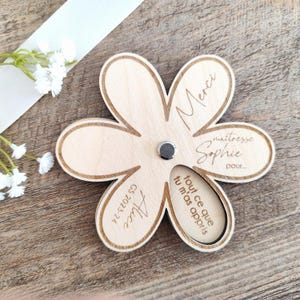 May include: A wooden flower-shaped magnet with a light brown finish. The magnet has six petals and features engraved text, including "Merci", "ma&icirc;tresse Sophie", and "Alice GS 2023-24". A small, round magnet is in the center.